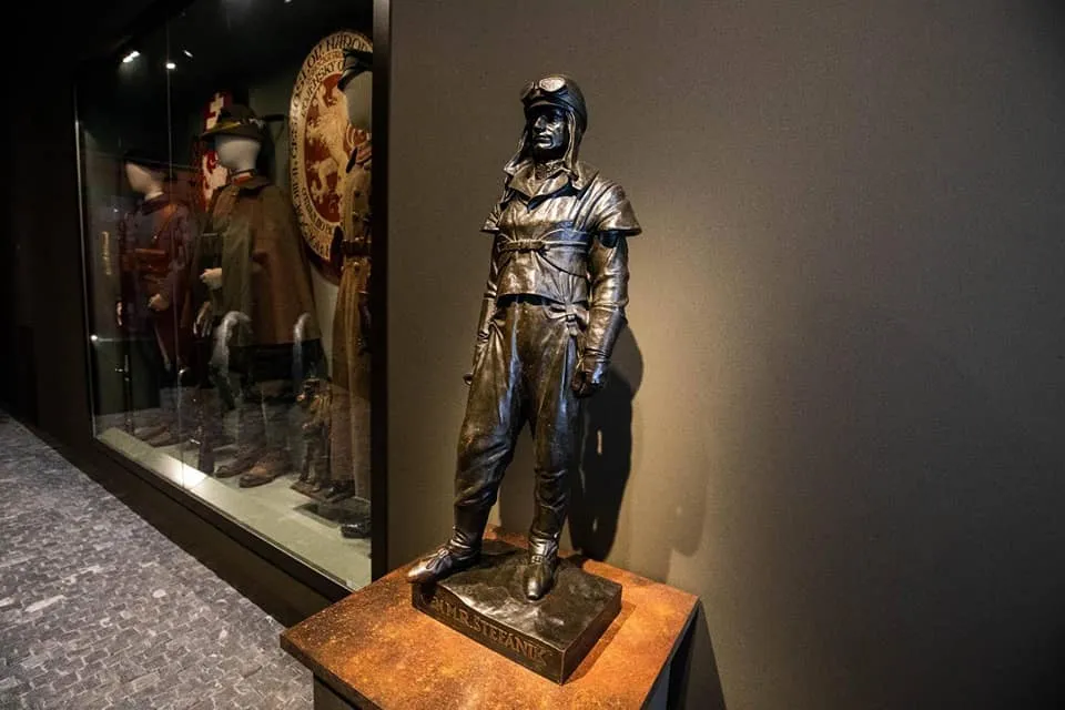 Bronzen standbeeld van een piloot in uniform, staande op een houten sokkel in een museumgalerij