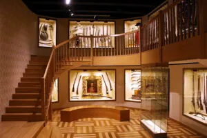 Interieur van een museum met een houten trap, glazen vitrines en tentoonstellingen aan de muren