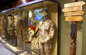 Militaire uniformen en uitrusting tentoongesteld in vitrines met richtingaanwijzers in de buurt
