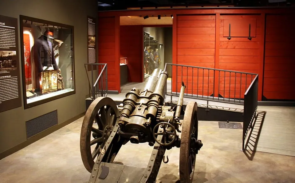 Een groot artilleriekanon tentoongesteld in een museumgalerij met een uniformtentoonstelling in een glazen vitrine en rode muren