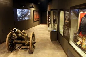 Een kanon tentoongesteld in een museumgalerij met vitrines en kunstwerken aan de muren