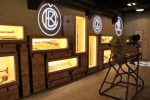Interieur tentoonstellingsruimte met houten vitrines, verlichte artefacten en cirkelvormige logo's aan de muur