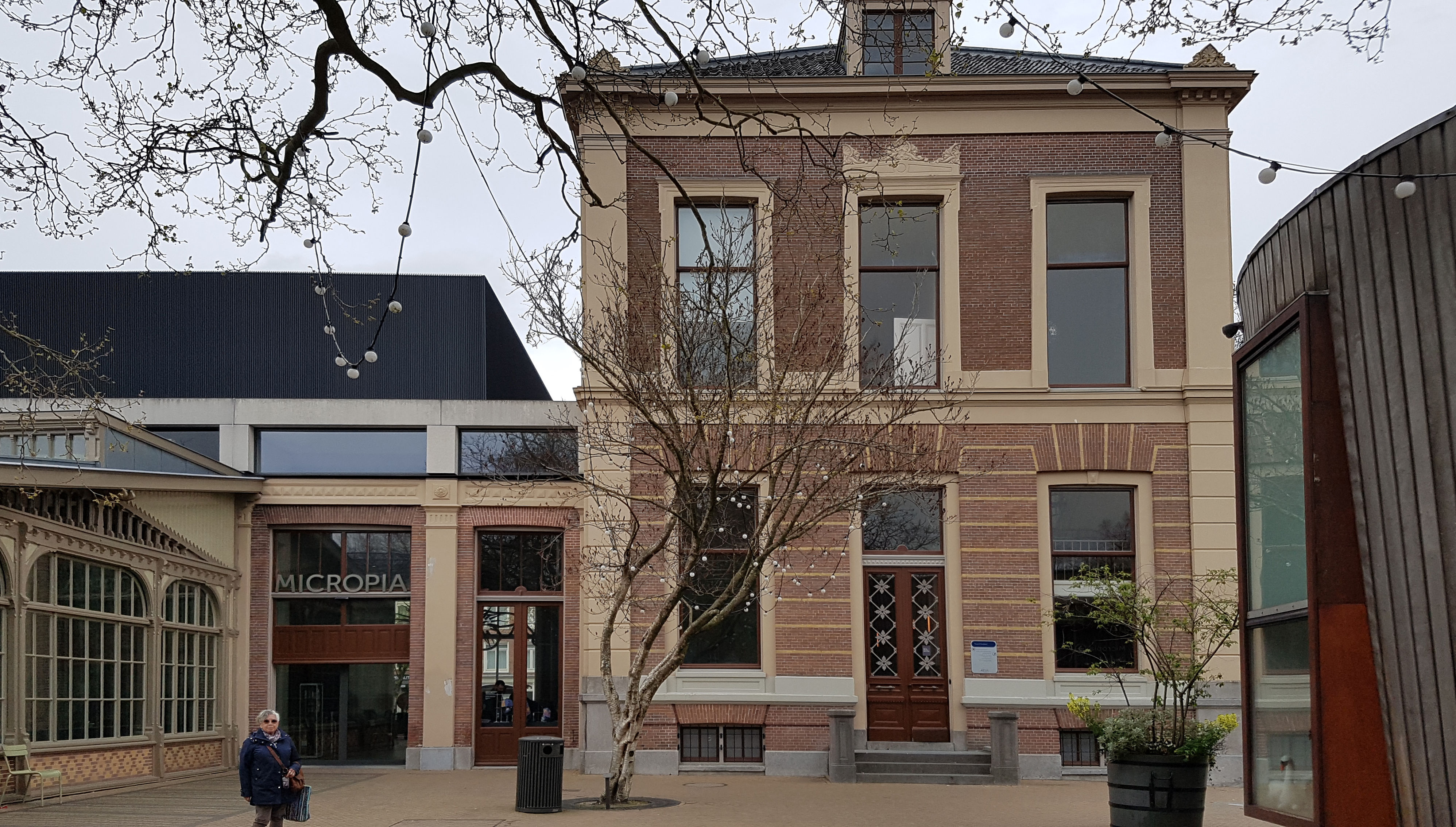 Buitenaanzicht van het Micropia-museumgebouw met een bakstenen gevel, boogvormige ramen en een bord met 'MICROPIA' boven de ingang.