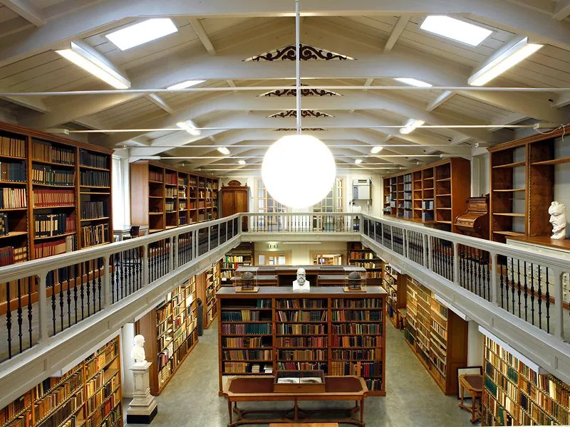 vista interior de una biblioteca con techos altos abovedados, estanterías de madera y una gran lámpara esférica