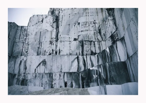 Fotografía a gran escala de una espectacular cara de cantera de mármol con paredes de corte vertical, vetas de agua oscura y pequeñas figuras humanas en la base para dar escala