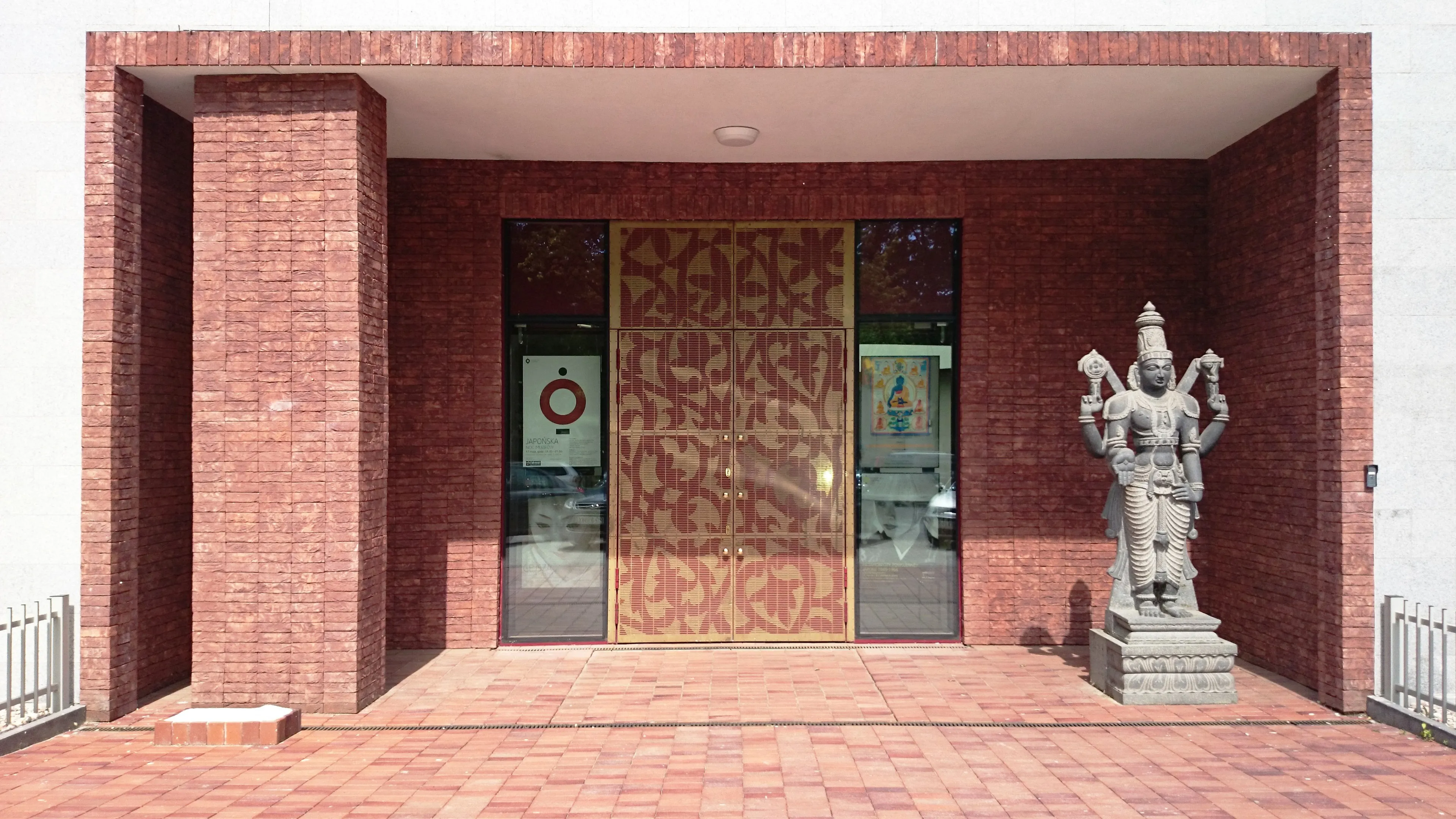 Entrada de un edificio de ladrillo rojo con una puerta de madera decorativa y una estatua de piedra de una deidad a la derecha