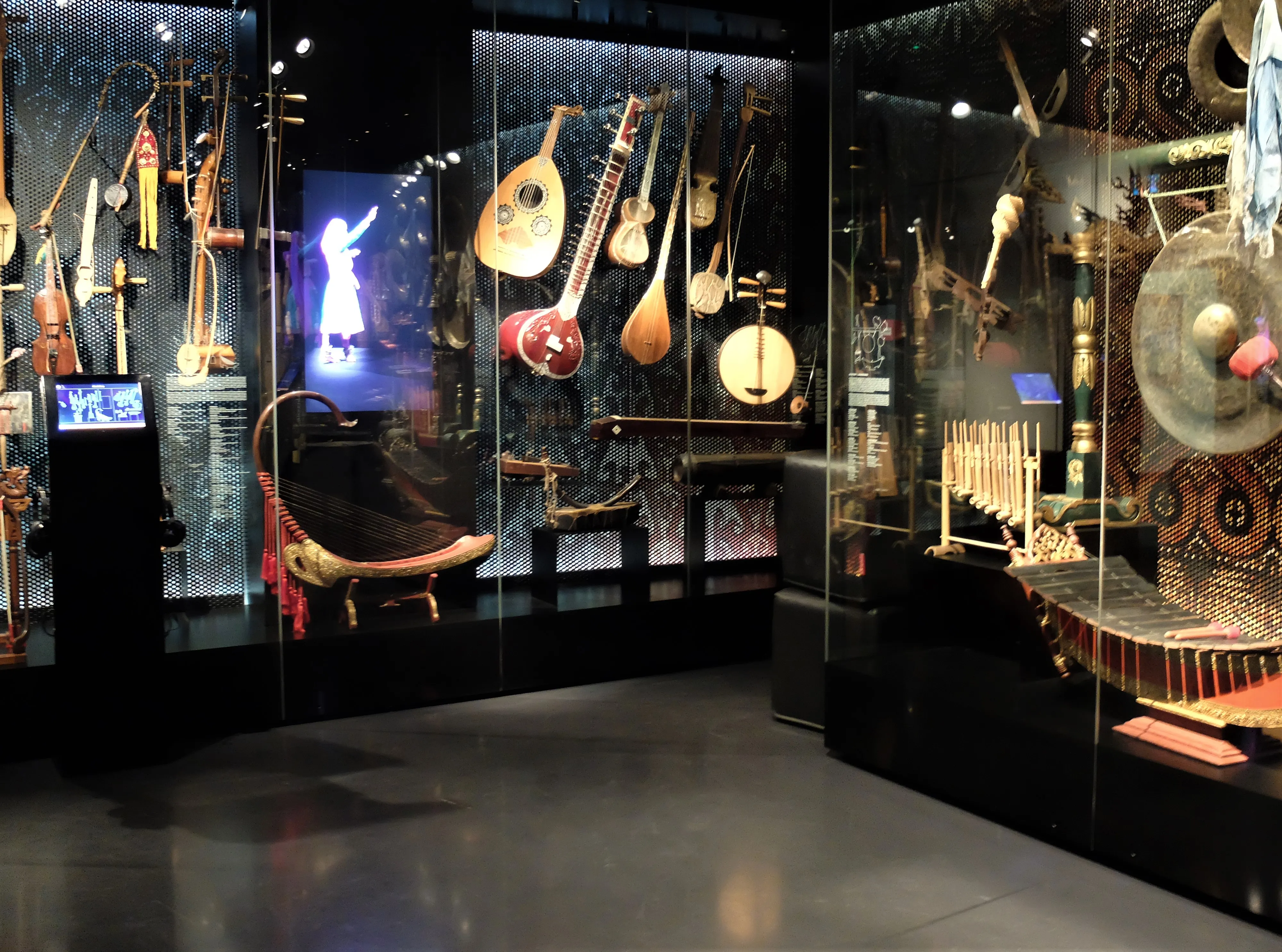 vitrinas de cristal que contienen varios instrumentos musicales tradicionales de Asia y Oceanía, incluidos instrumentos de cuerda y un gran gong, en una galería de museo