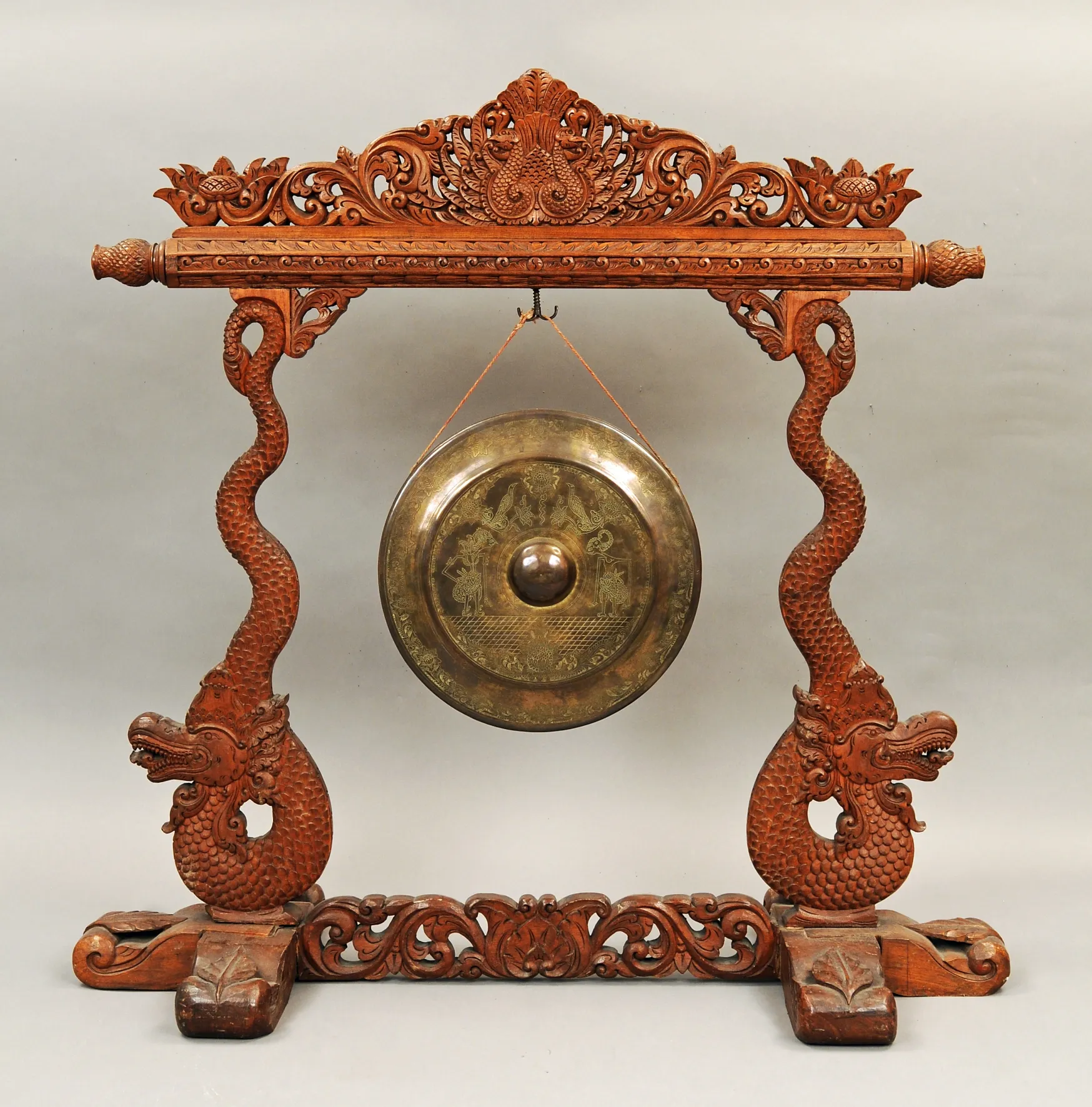 Un gong de bronce colgado de un ornamentado soporte de madera con dragones tallados y motivos florales
