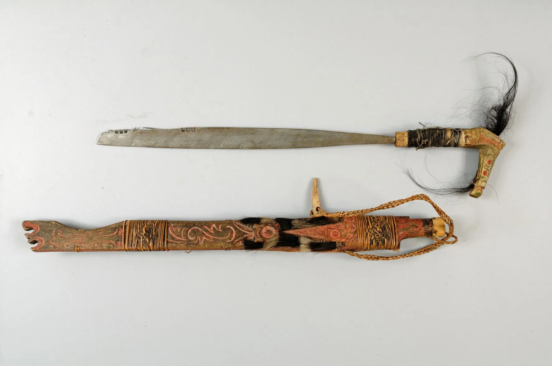 Een traditioneel Tasak Parang-mes met een gebogen lemmet en een sierlijk handvat, tentoongesteld naast de ingewikkeld gesneden schede met een gevlochten koord