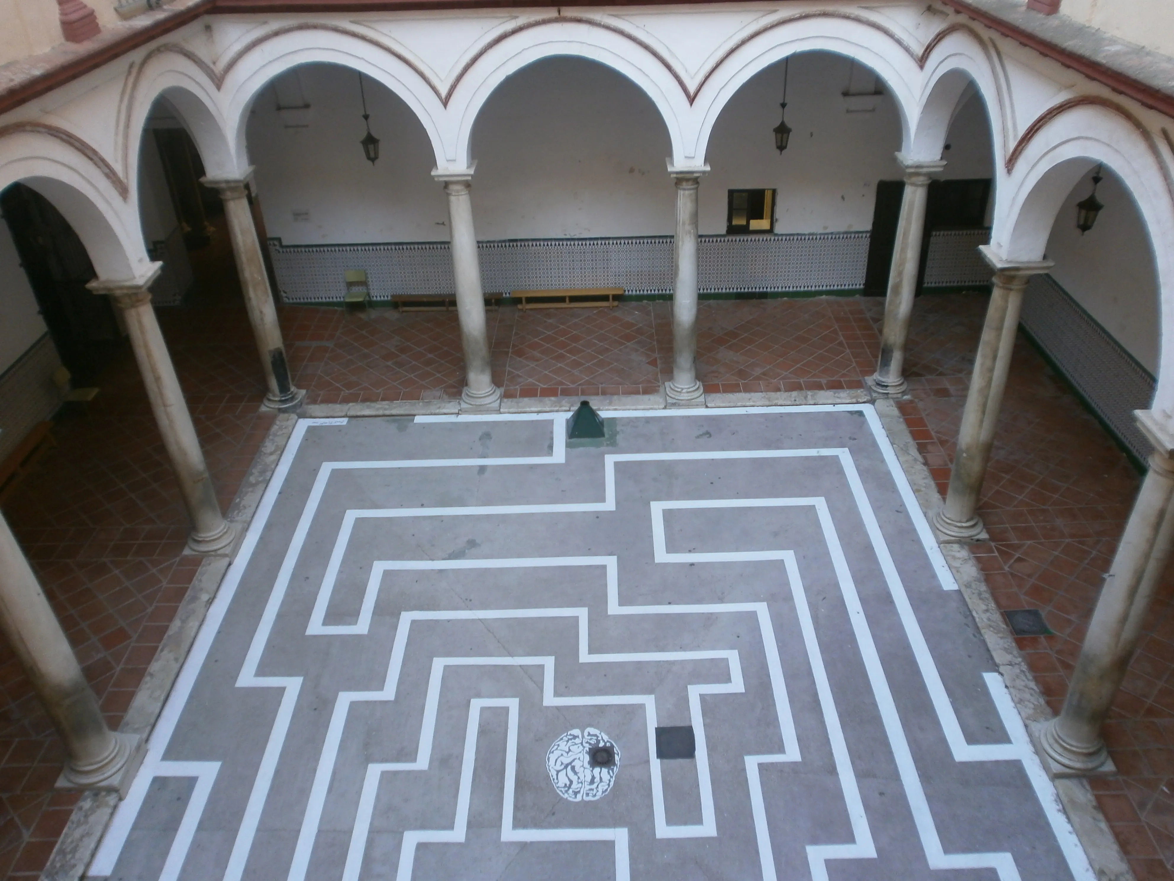 Patio interior del Ateneo de Málaga con una columnata blanca arqueada que rodea un gran patrón de laberinto blanco pintado en el suelo gris