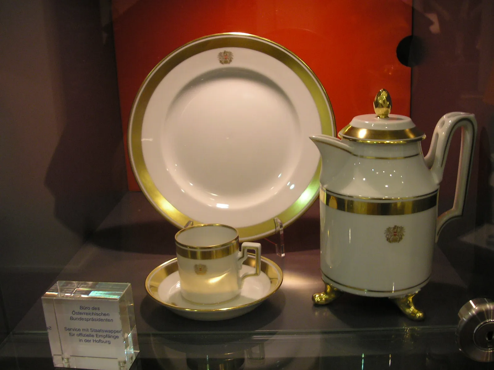 Tetera, taza, platillo y plato de porcelana blanca y dorada expuestos en una vitrina de cristal