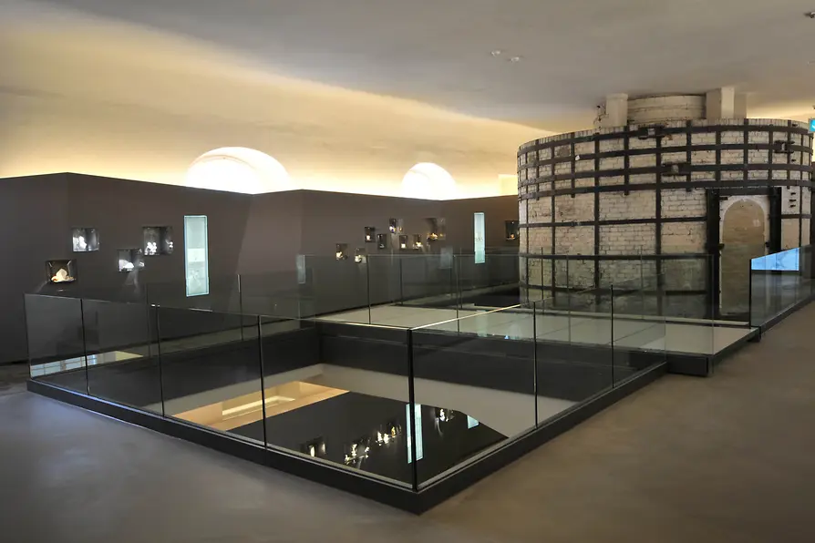 Interior de un museo con vitrinas de cristal y una gran estructura de horno cilíndrico