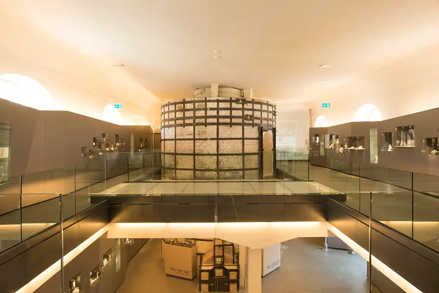 Interior de un museo con barandillas de vidrio, una vitrina cilíndrica central e iluminación cálida