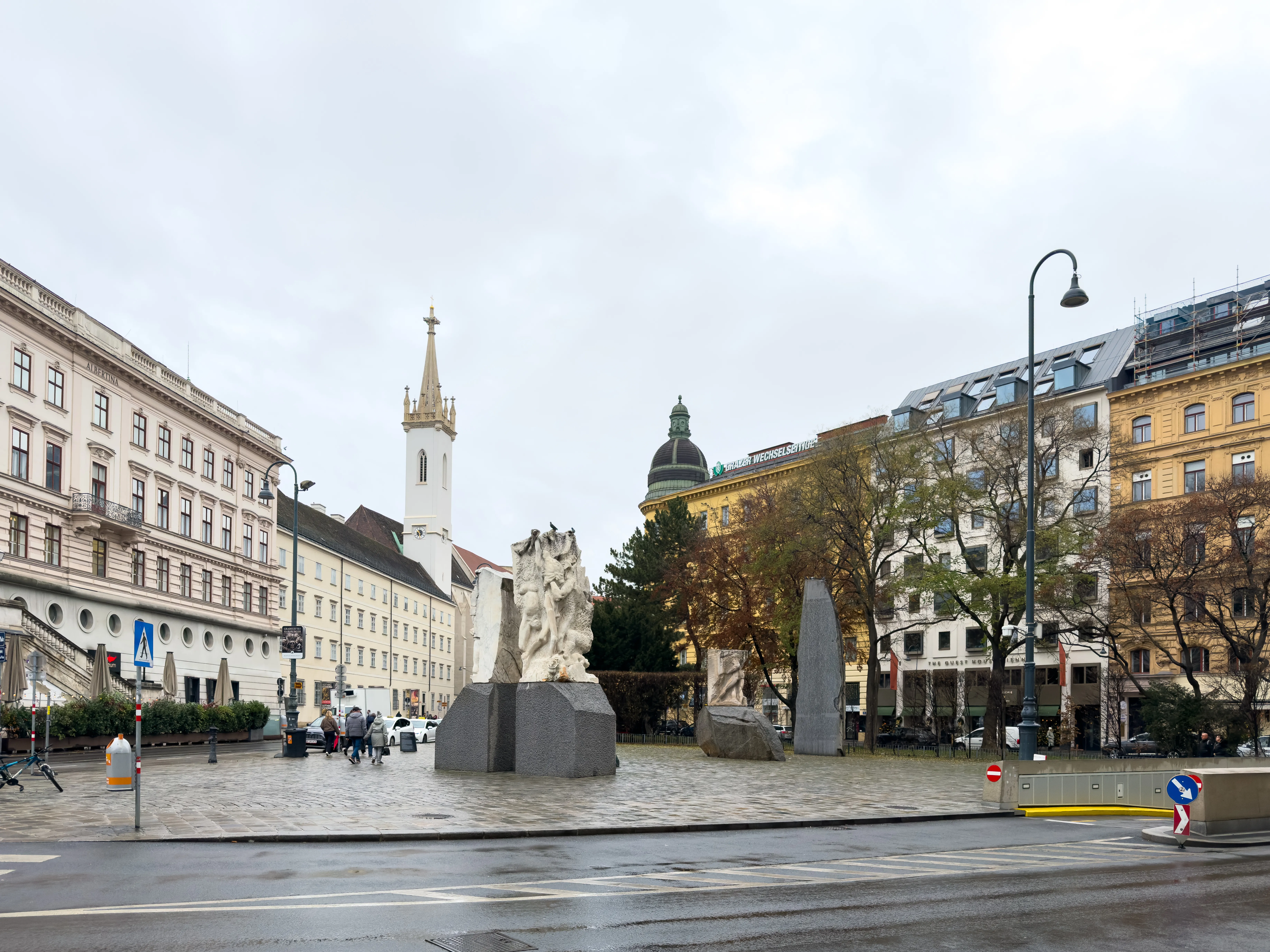 The Church of the Augustinian Friars with its spire visible behind a public square featuring a modern sculpture and surrounding buildings