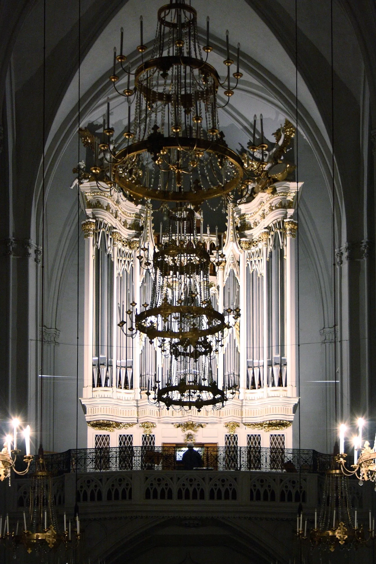 Ornate pipe organ with gold detailing and large chandeliers inside a church with arched ceilings