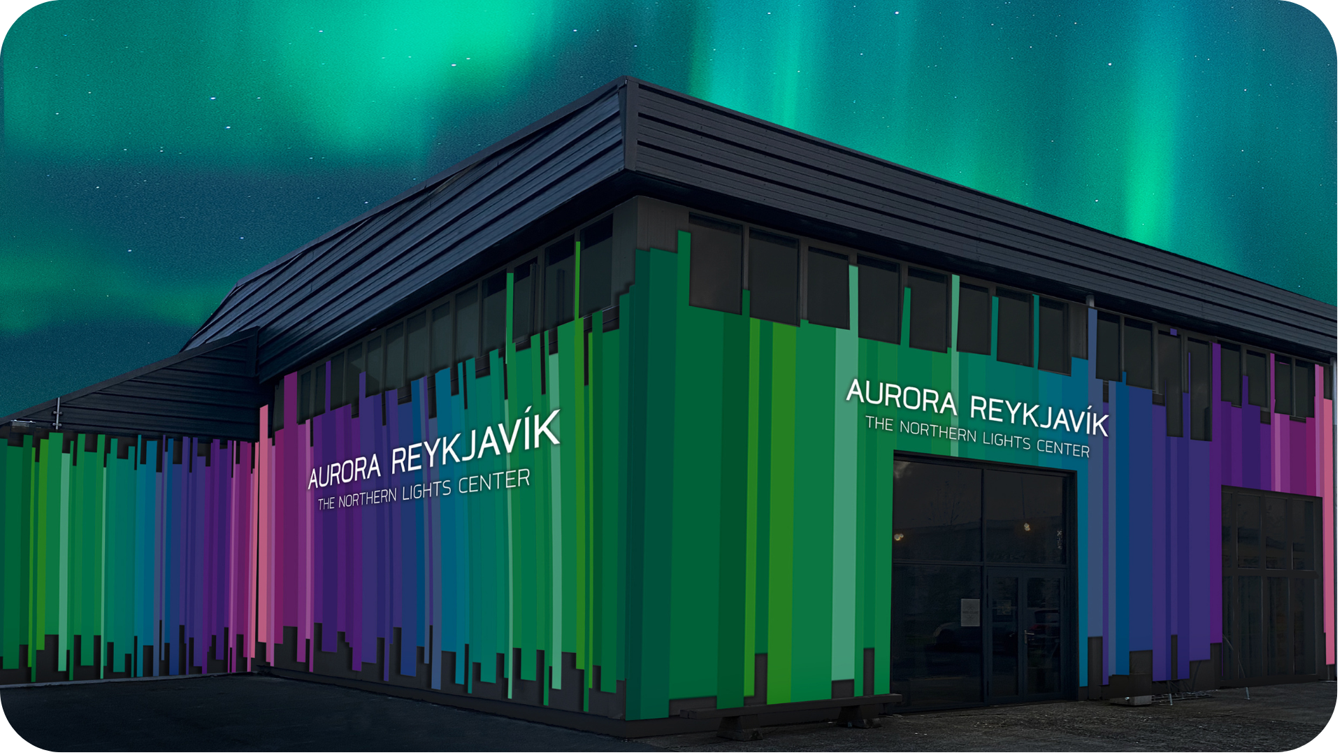 Fasada budynku Aurora Reykjavík Northern Lights Center z kolorowymi pionowymi pasami w odcieniach zieleni, błękitu i fioletu na tle nocnego nieba z zorzą polarną