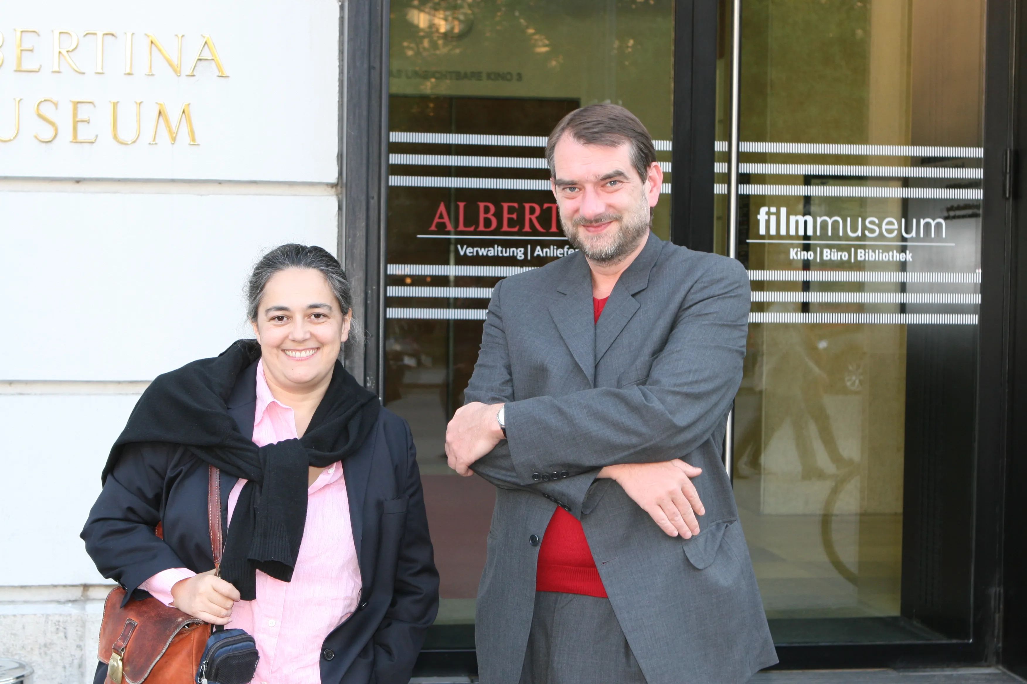 Two people standing in front of the entrance to the Austrian Film Museum, with signage on the glass doors and wall.