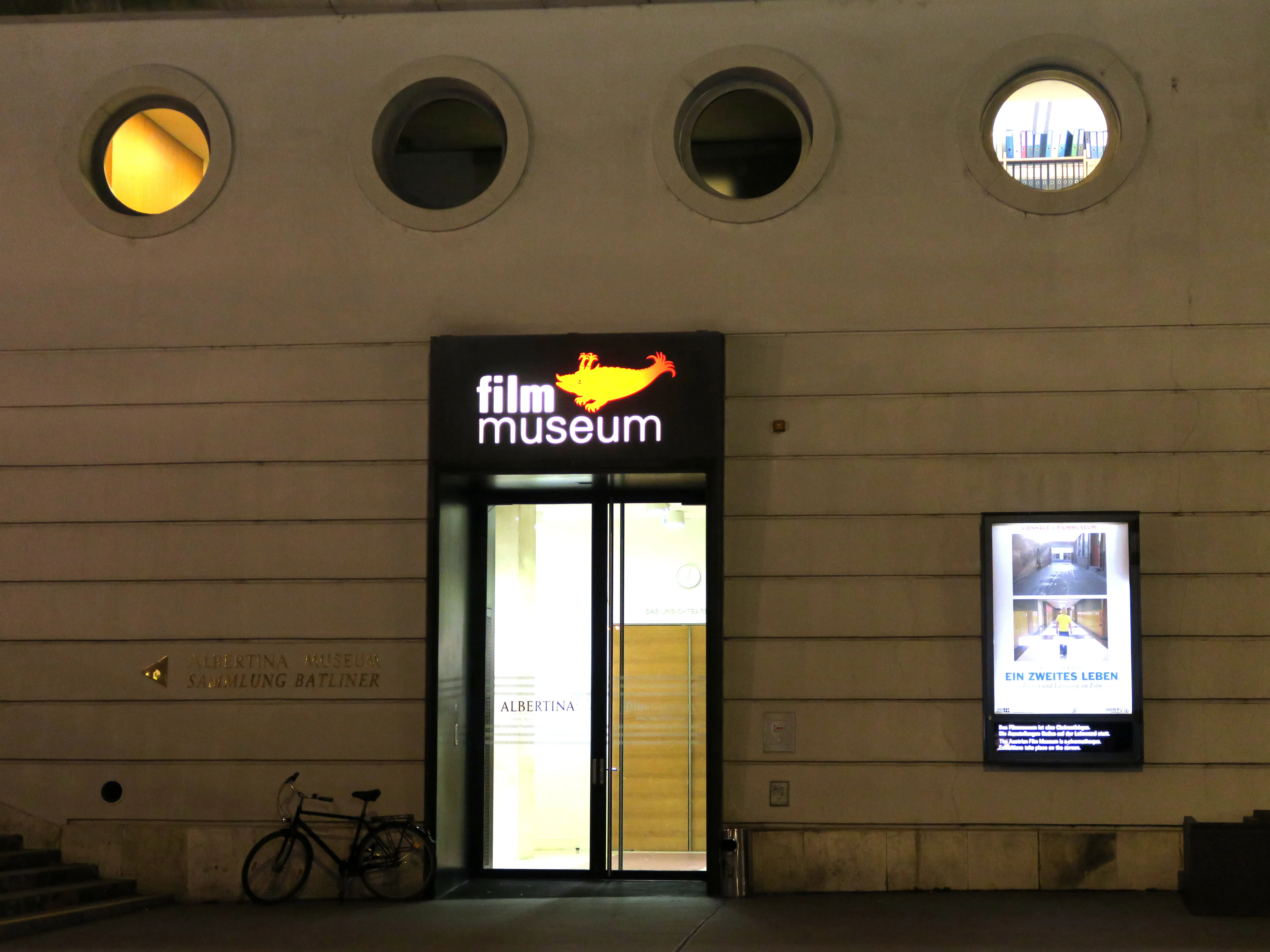Entrance to the Austrian Film Museum at night with a lit sign and circular windows