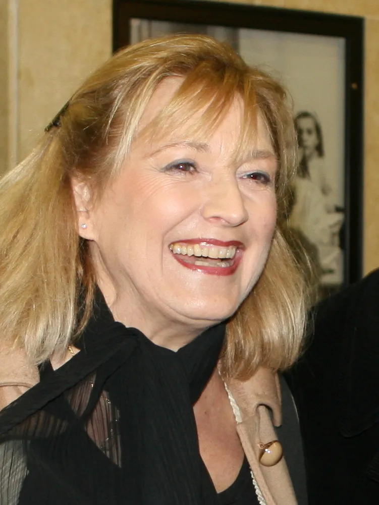woman with blonde hair smiling in front of a framed photograph