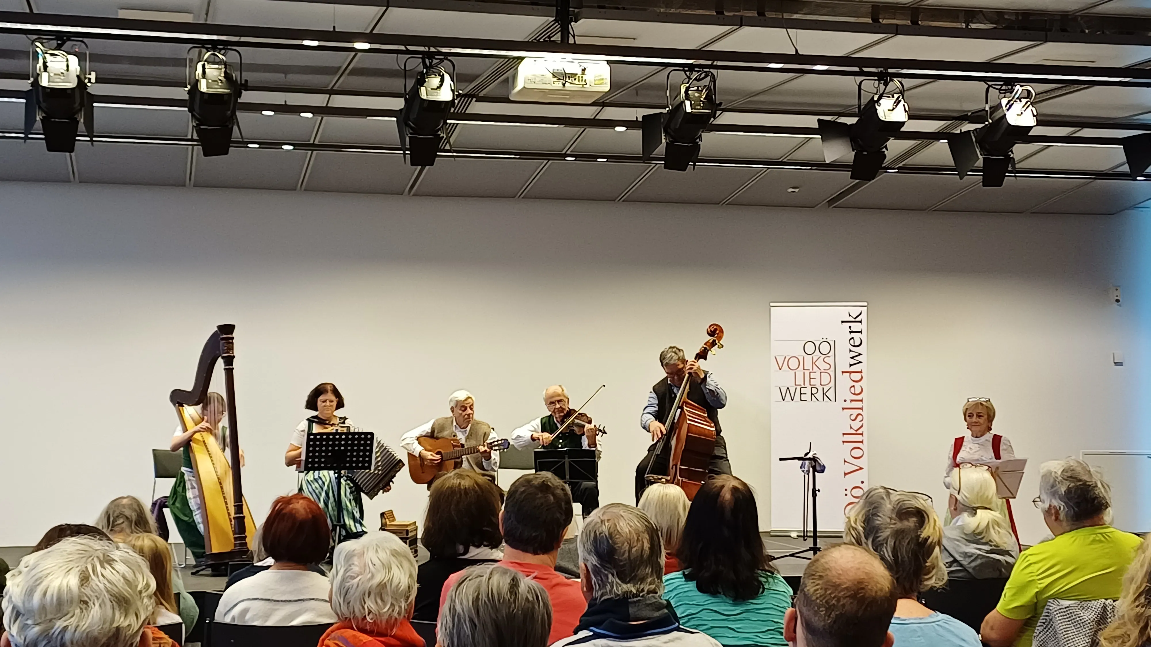 Músicos actuando en el escenario con una pancarta que dice 'Österreichisches Volksliedwerk' detrás.