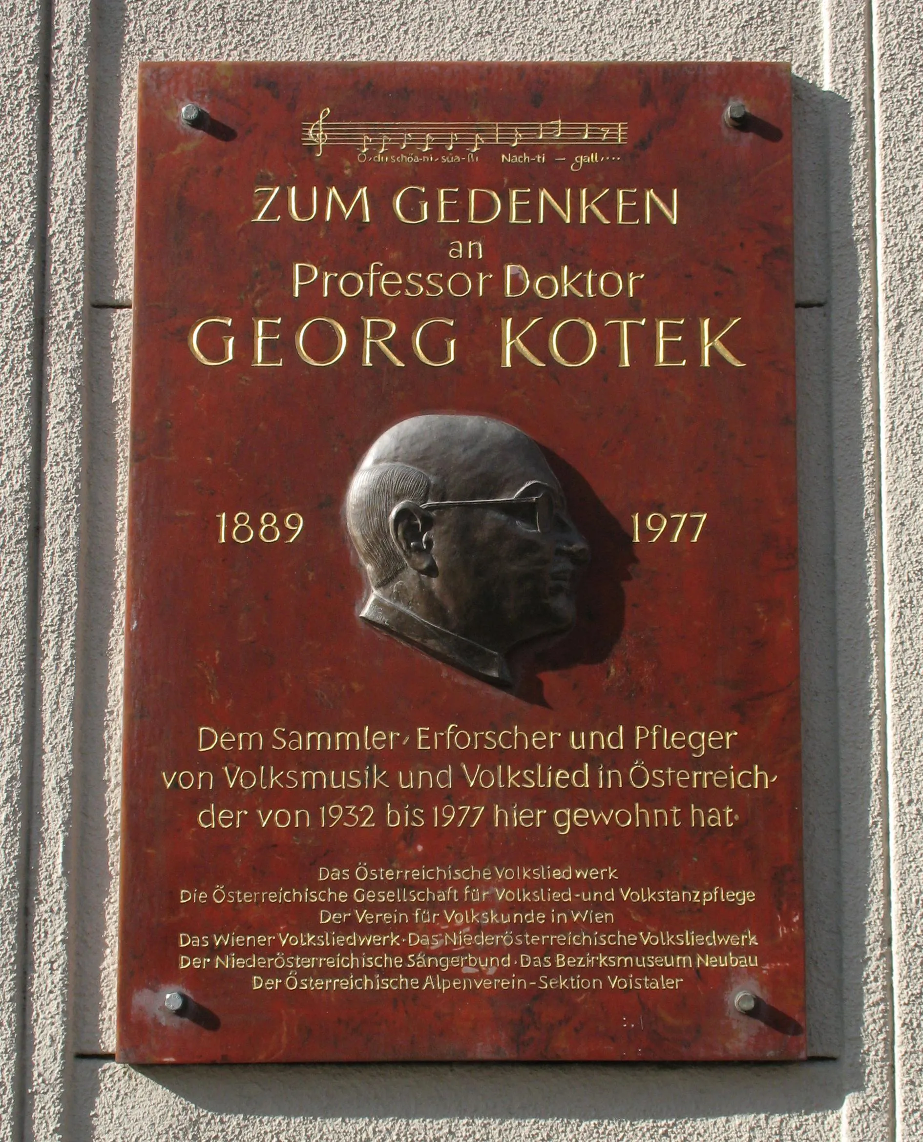 placa roja con letras doradas y un retrato en relieve de un hombre, montada en una pared
