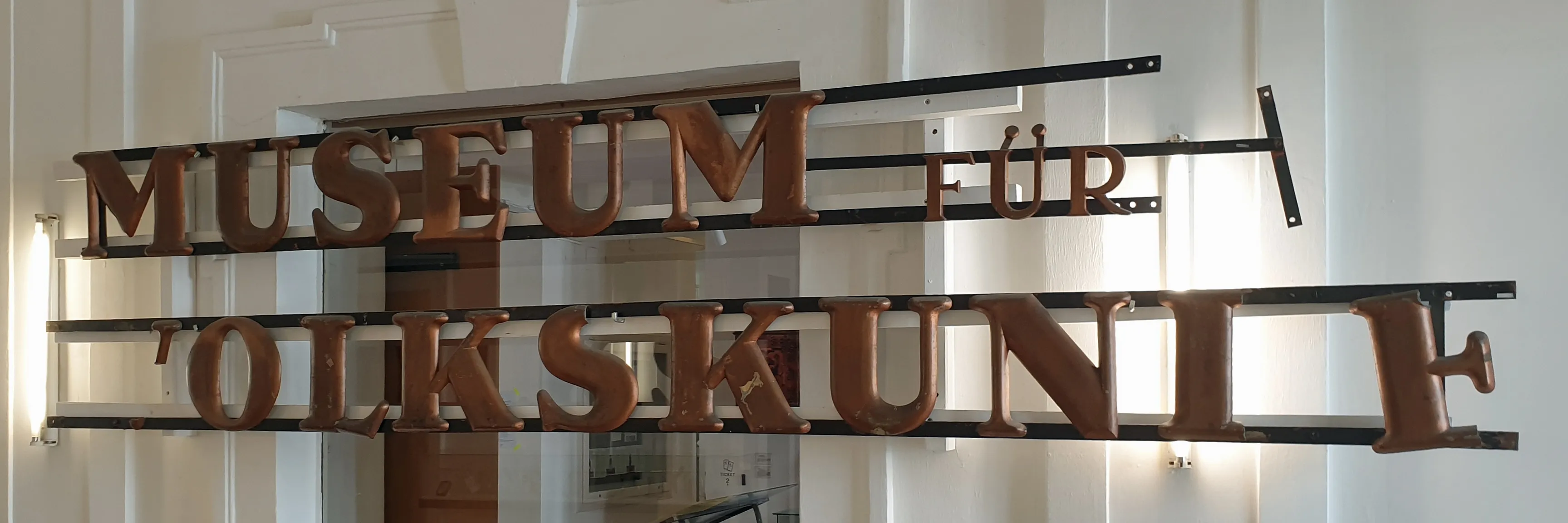 Letrero de metal con letras en relieve que deletrean 'MUSEUM FÜR VOLKSKUNDE' en alemán