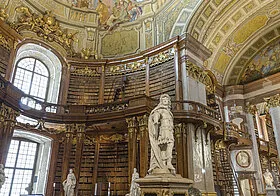 Bogato zdobione wnętrze Austriackiej Biblioteki Narodowej z drewnianymi regałami, centralną statuą i ozdobionym sufitem
