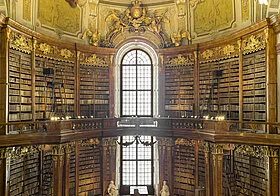 interior de una gran biblioteca con altas ventanas arqueadas, techos ornamentados dorados y hileras de estanterías