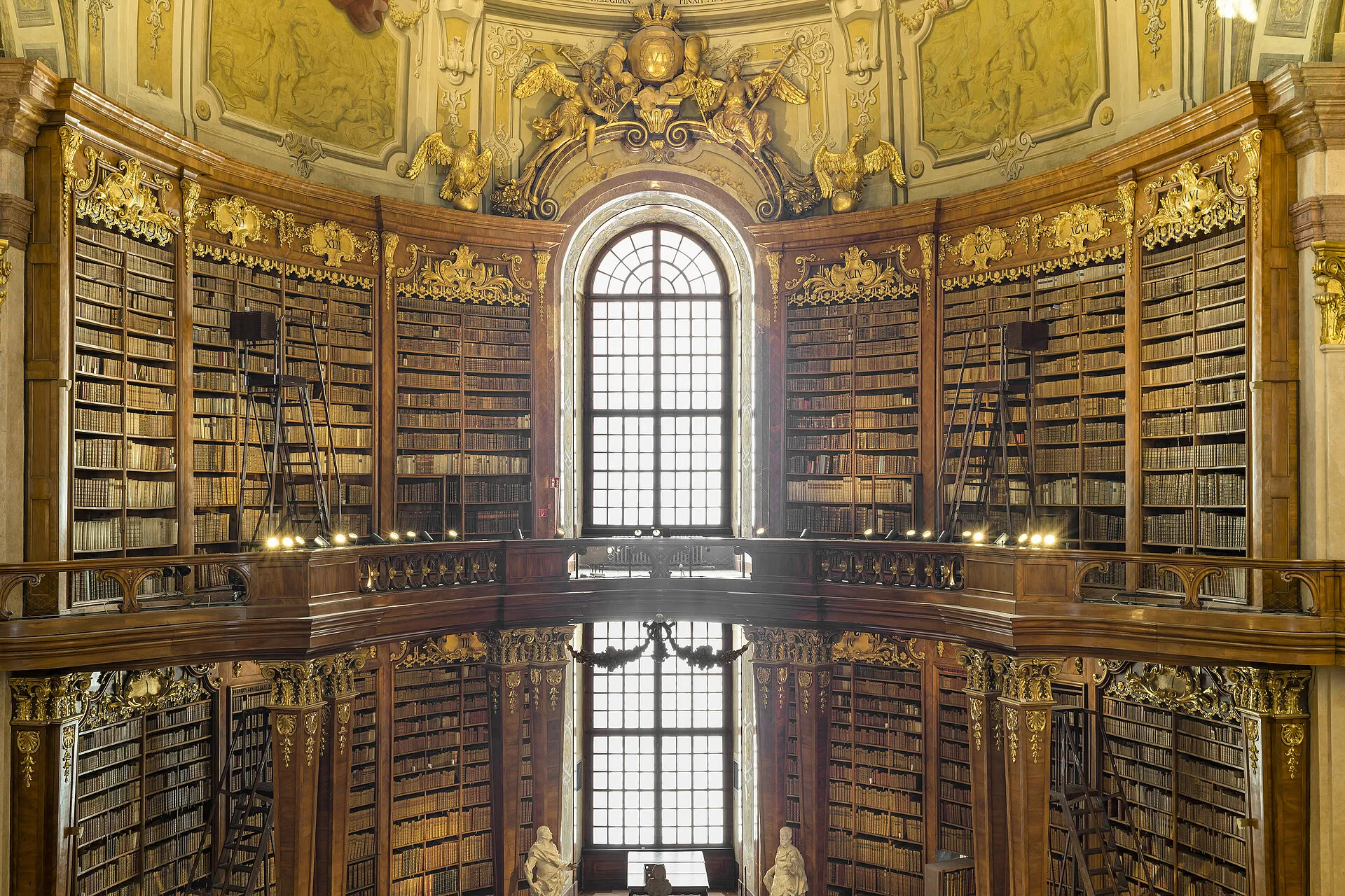 Interior de biblioteca ornamentado con estanterías de madera, decoraciones doradas y una gran ventana arqueada que se refleja en un suelo pulido