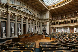 Interieur van het Oostenrijkse parlementsgebouw met rijen houten stoelen, klassieke zuilen en een glazen plafond