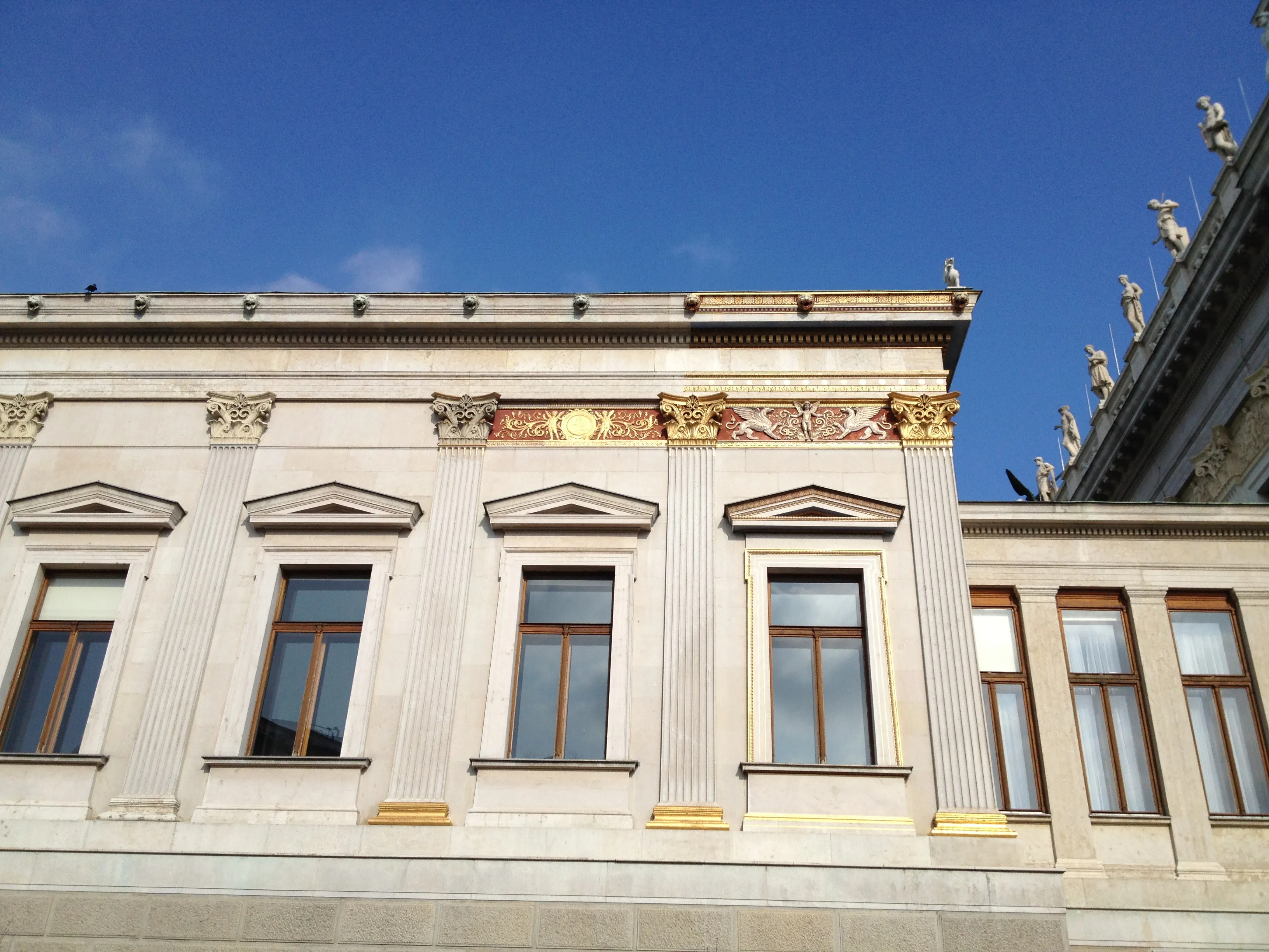 Neoclassicistisch gevel van het Oostenrijkse parlementsgebouw met gouden accenten en sierlijke details onder een blauwe hemel