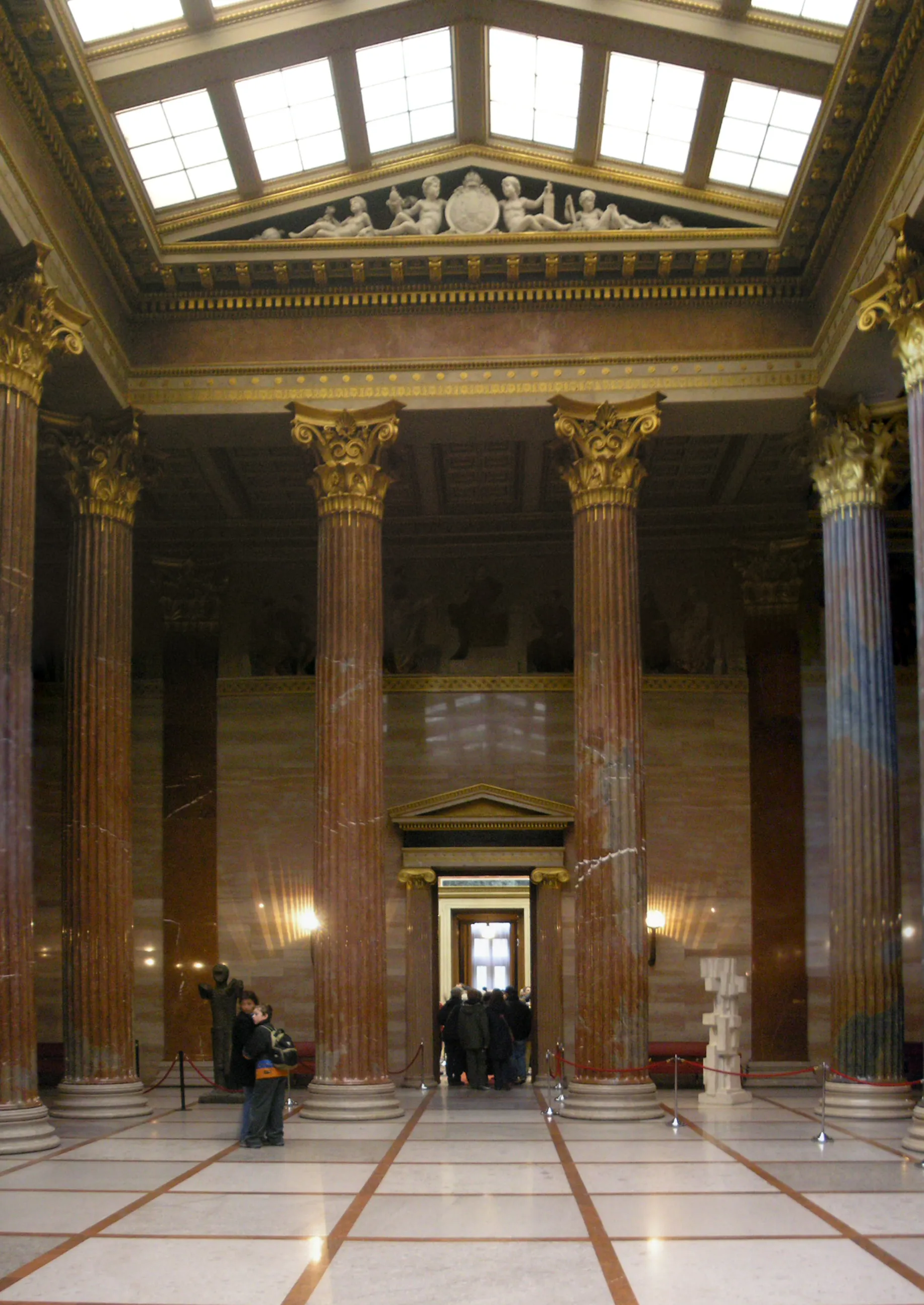 Interieur van een grote hal met hoge marmeren zuilen, een hoog plafond met daklichten en een gepolijste marmeren vloer