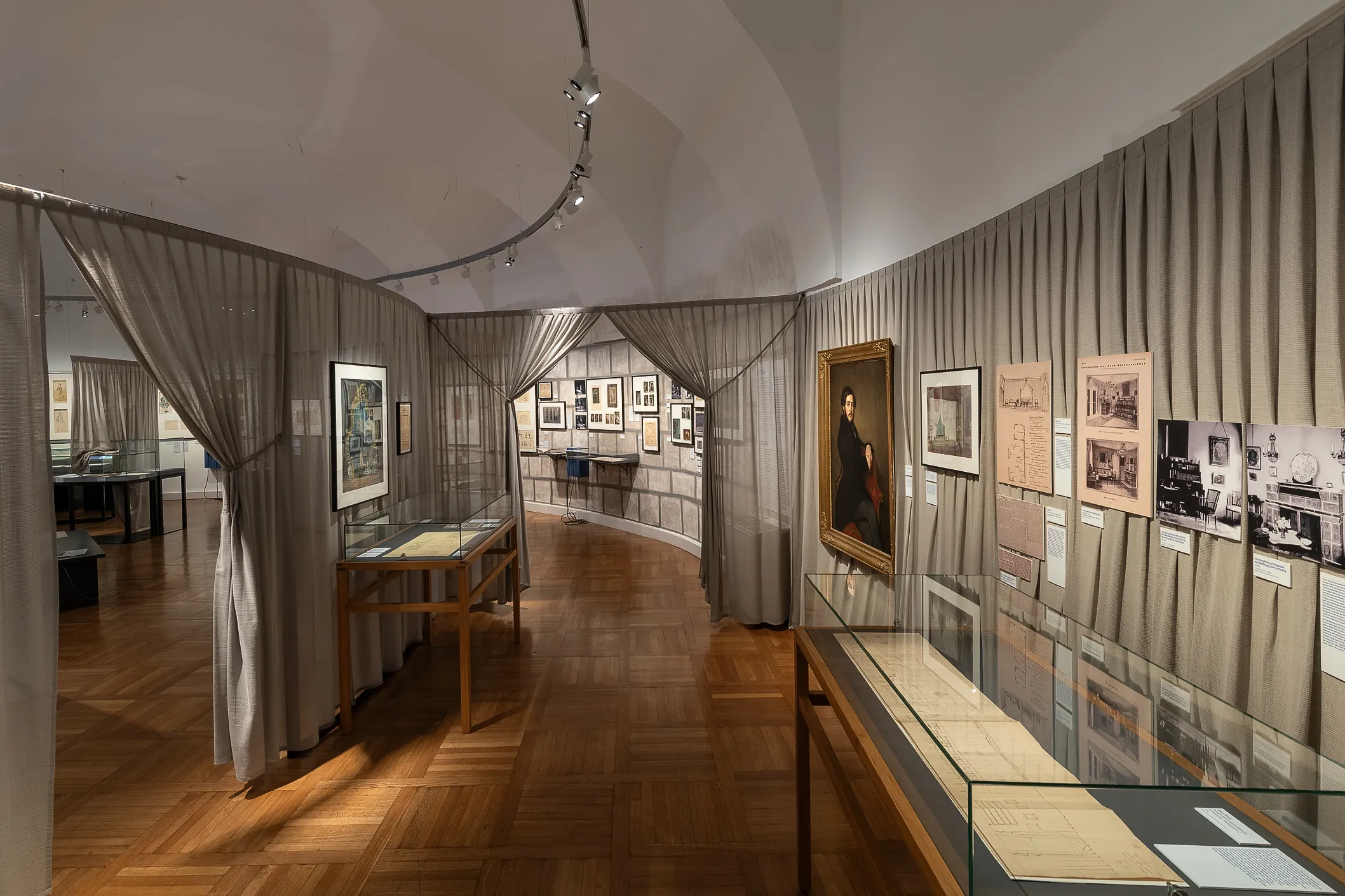Wnętrze Galerii Austriackiego Muzeum Teatralnego z drewnianymi podłogami, szklanymi gablotami i oprawionymi eksponatami na ścianach