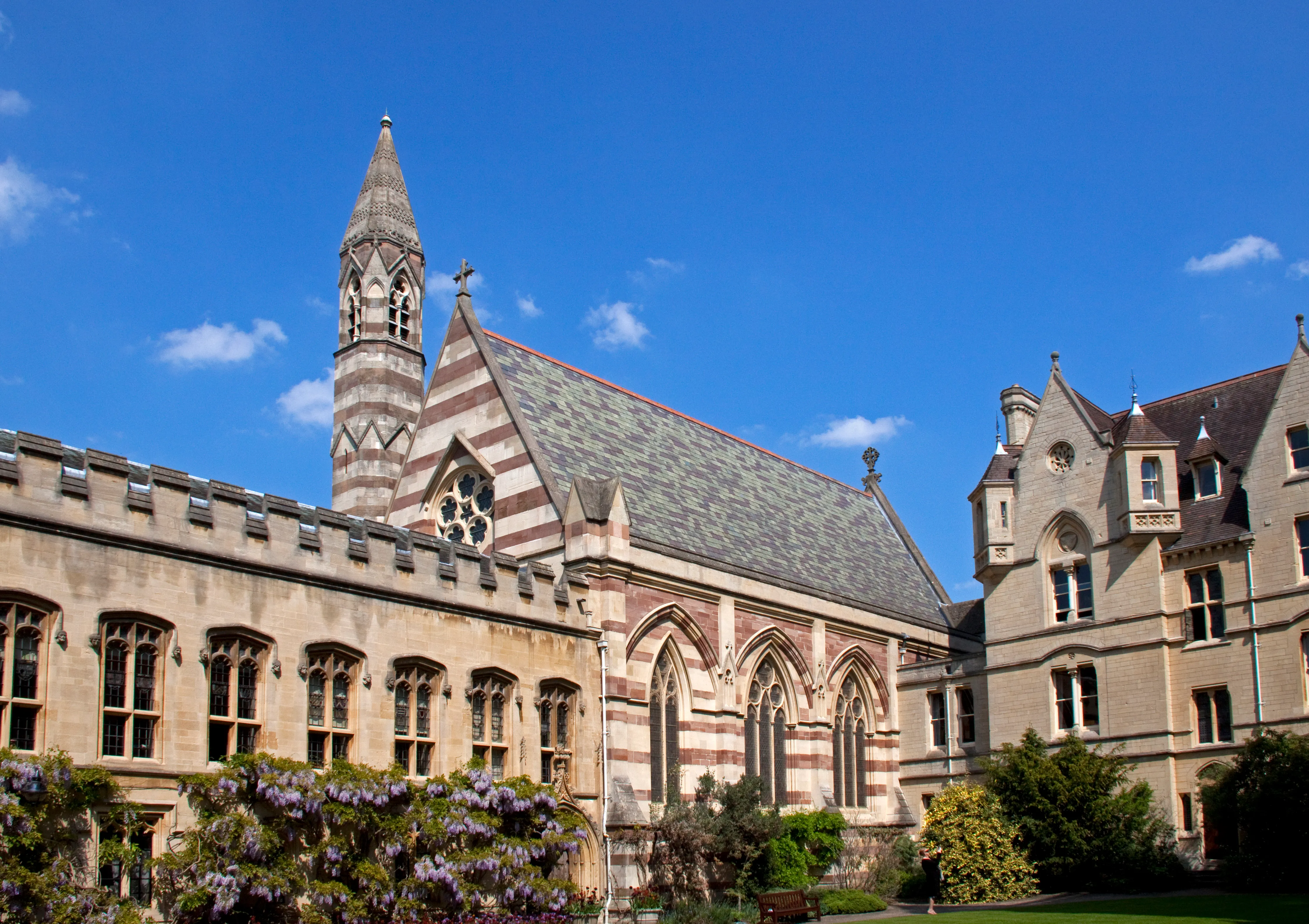 Vista exterior de la Balliol College Chapel que muestra una torre de piedra a rayas y ventanas góticas bajo un cielo azul.