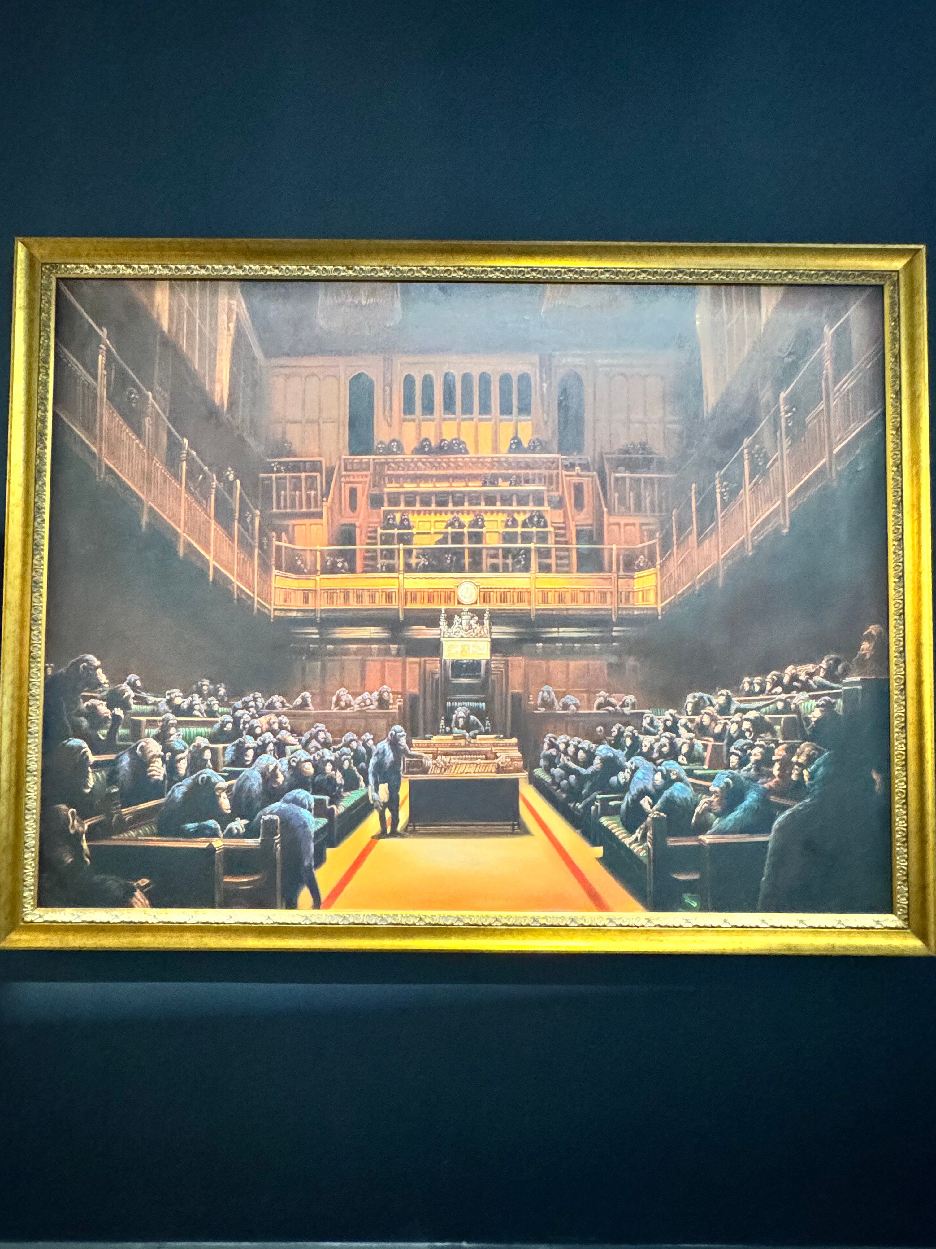 Pintura enmarcada de un interior de sala de tribunal abarrotada con balcones de madera, marco dorado, fondo de pared oscuro