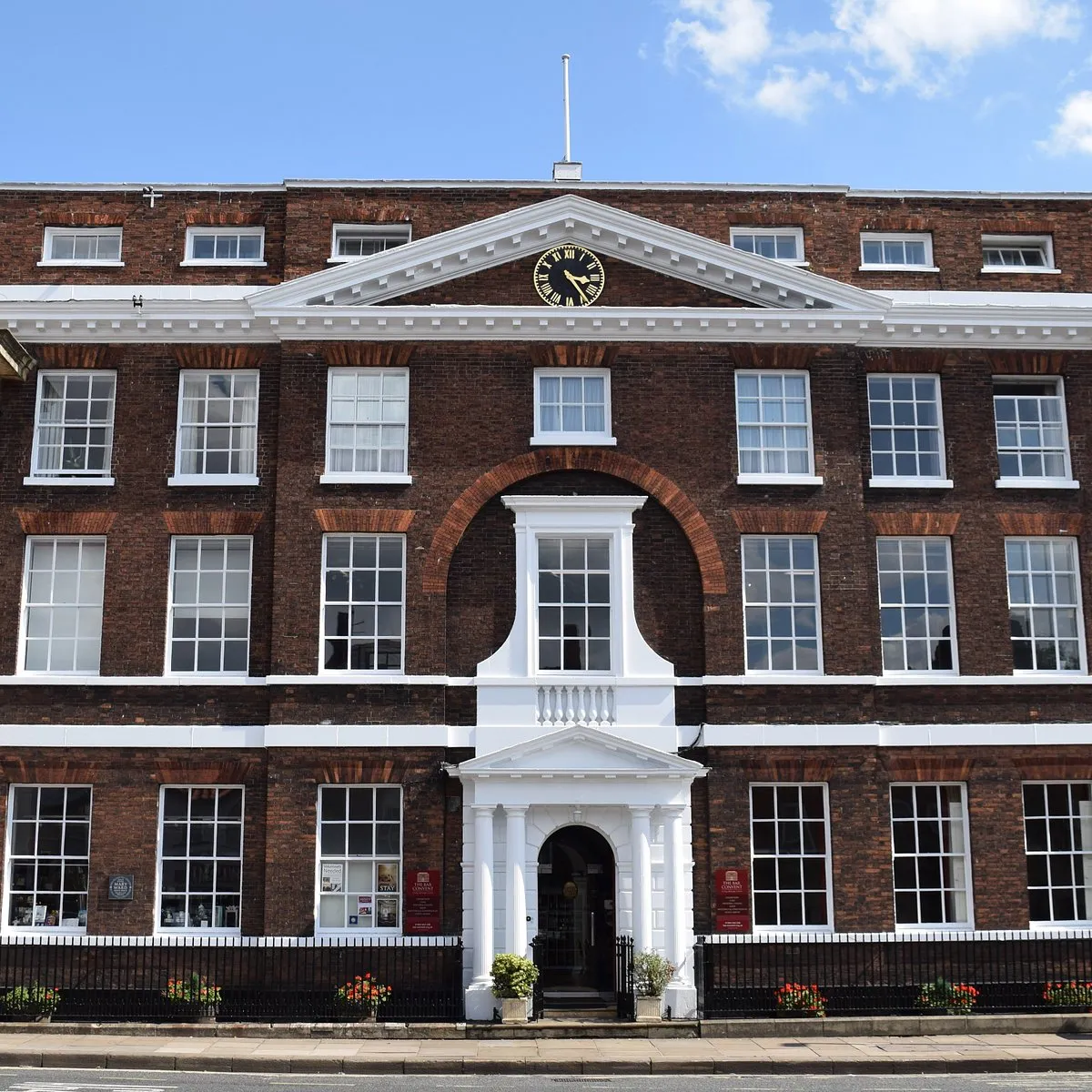 Red brick Georgian-style building facade with white trim, central portico entrance, and a clock in the triangular pediment