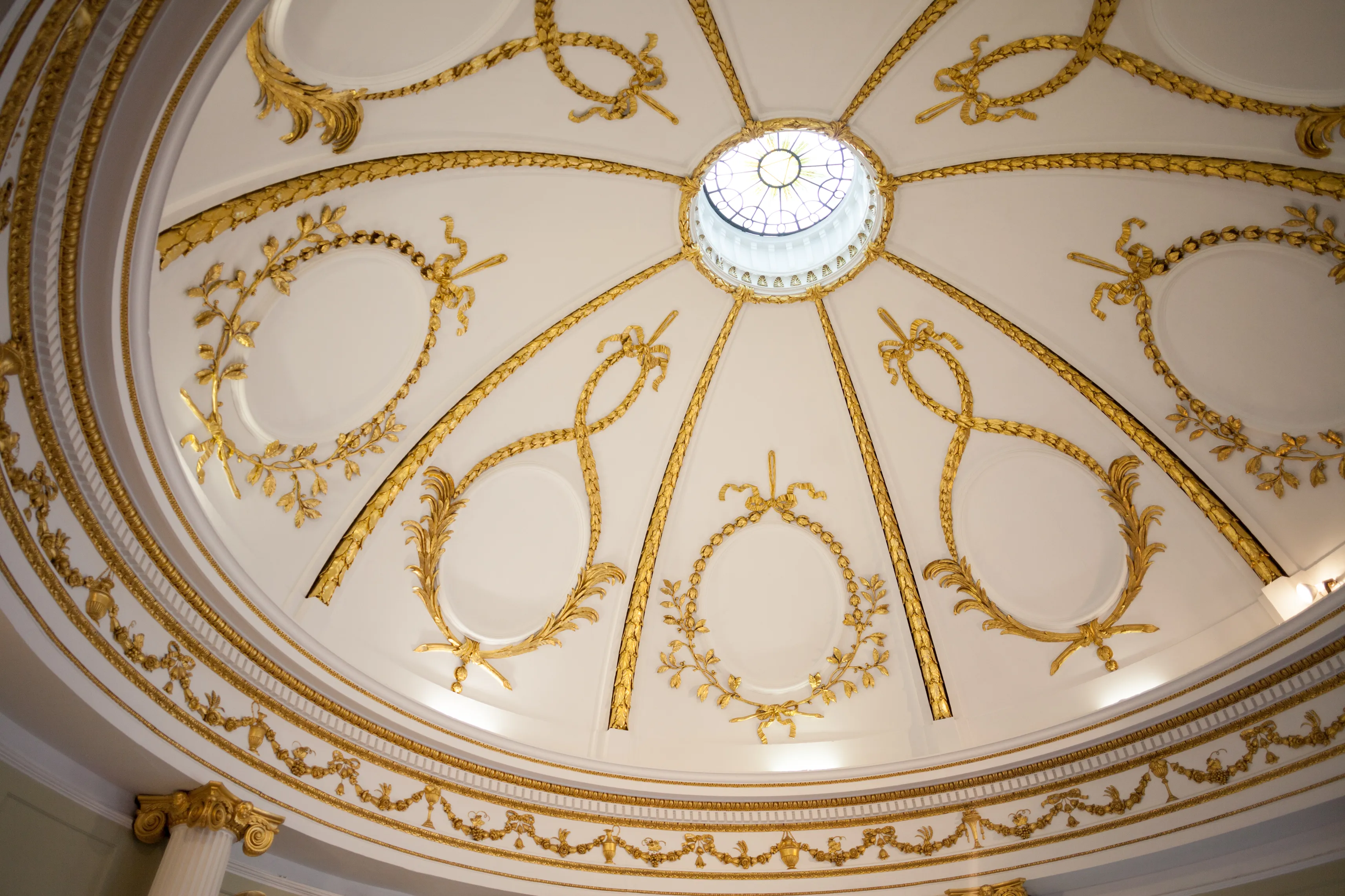 Ornate white and gold plasterwork dome ceiling with radiating ribs, decorative garland medallions, and a central circular skylight