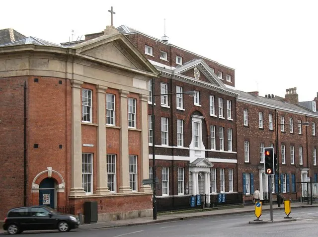 Red brick Bar Convent building with classical stone facade, pediment topped with a cross, and white entrance portico along a street