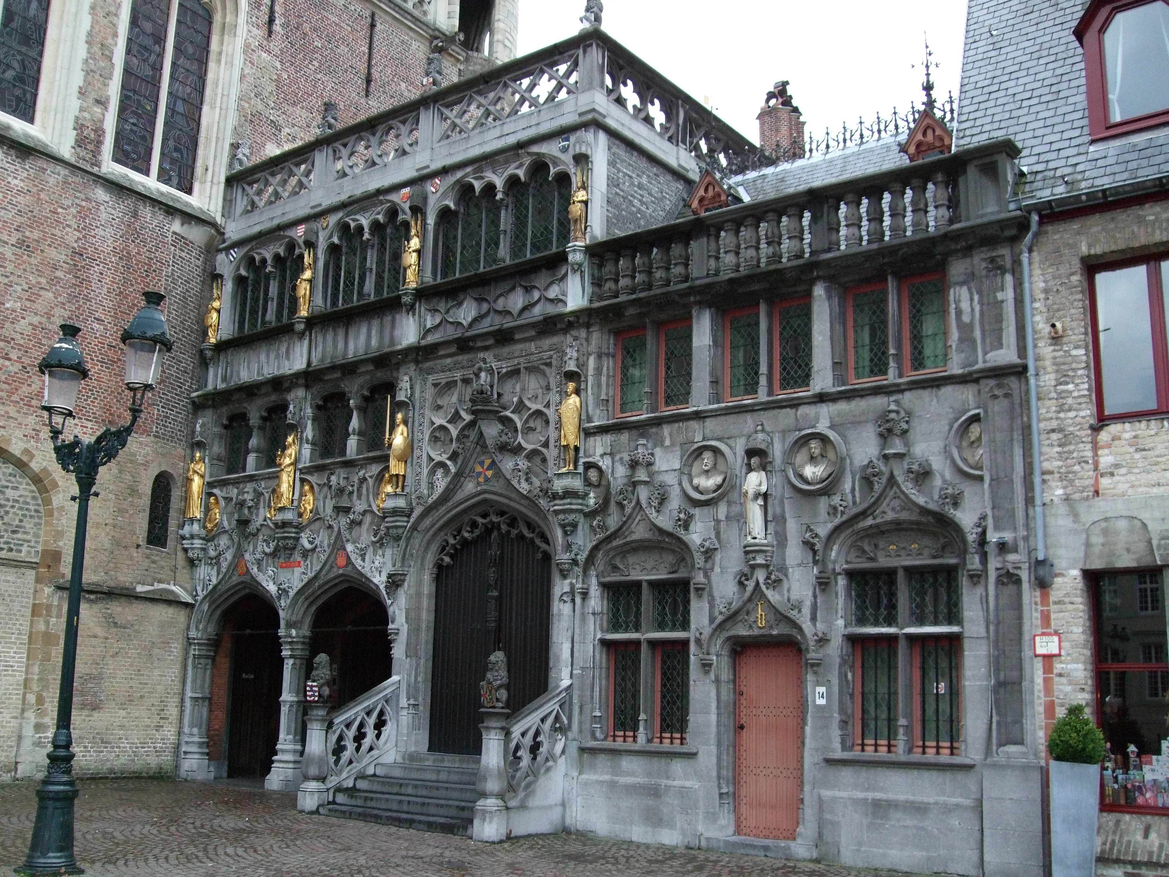 Gothic stone facade of the Basilica of the Holy Blood with golden statues, arched doorways, and ornate carvings on a cobblestone square