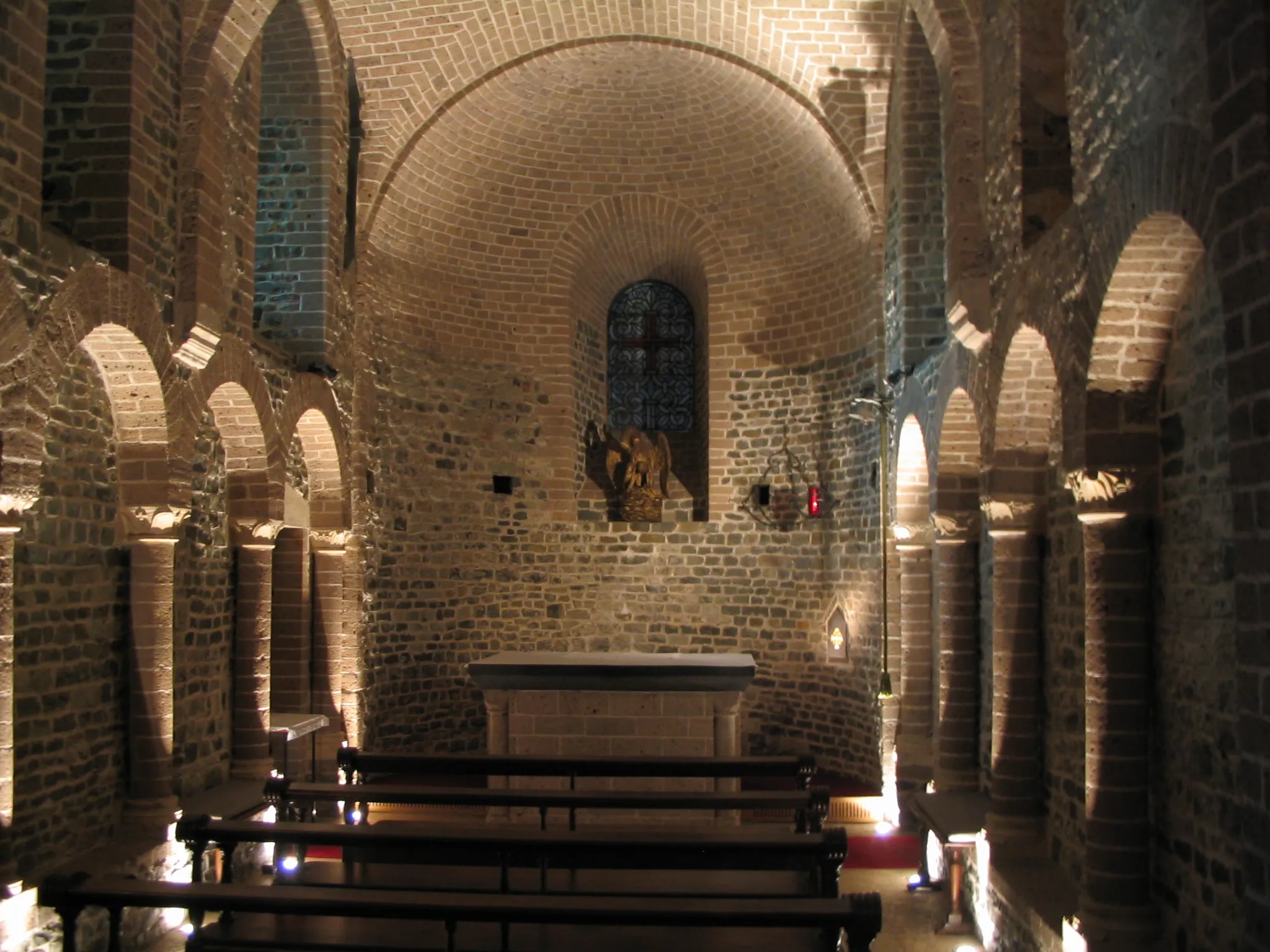 Interior of the Basilica of the Holy Blood showing Romanesque brick arches, stone columns, wooden pews, and an altar with a religious statue in a niche above it