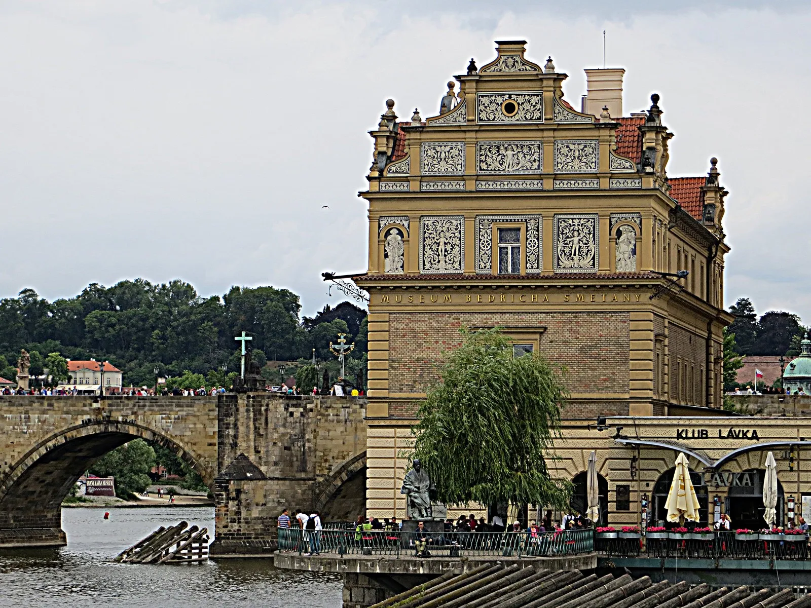 Budynek w stylu neorenesansowym z ozdobną fasadą nad brzegiem rzeki, kamienny most w tle