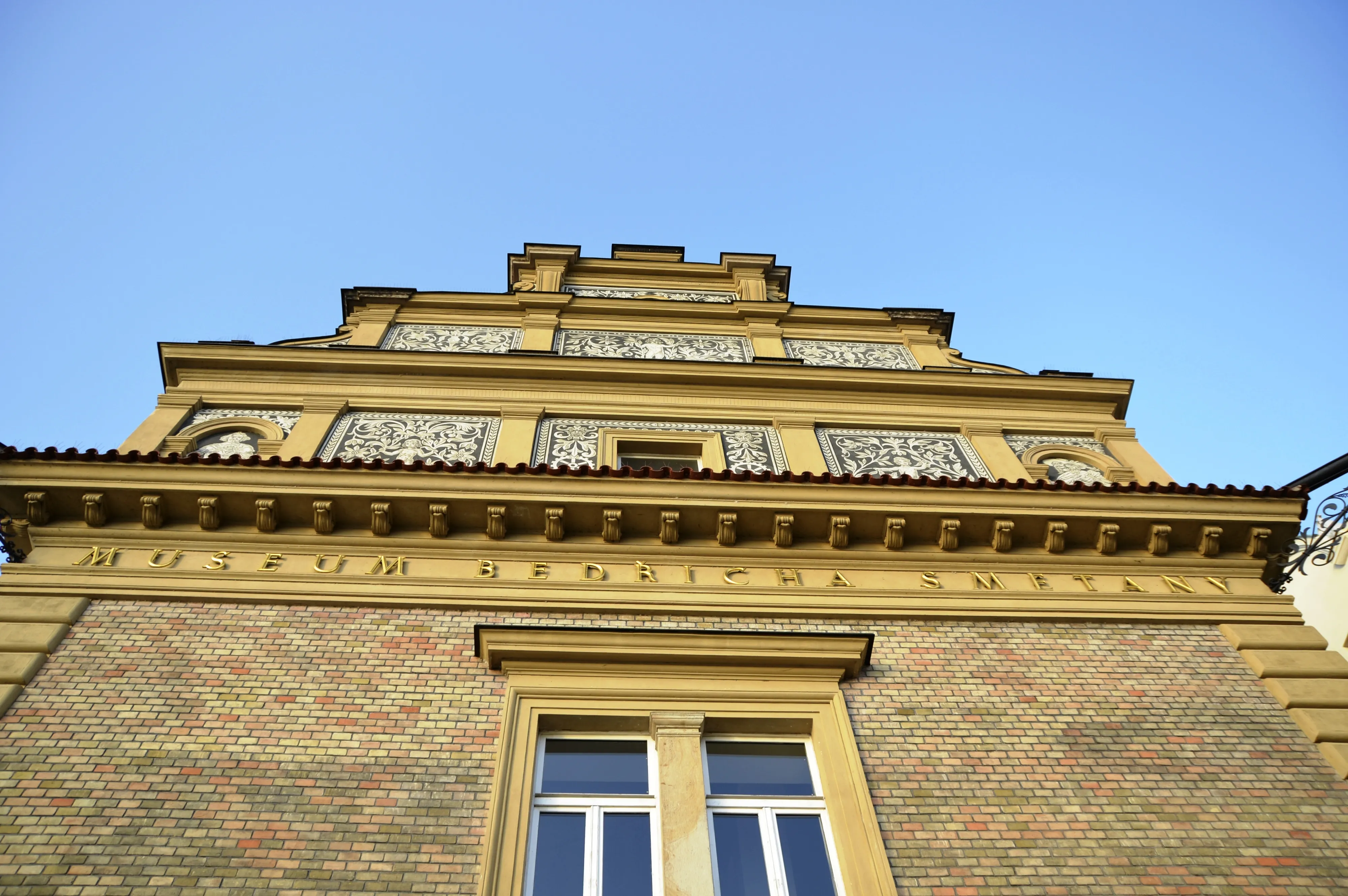 Neo-Renaissancistisch gebouw met bakstenen gevel en decoratieve tegelpanelen onder een stralend blauwe hemel