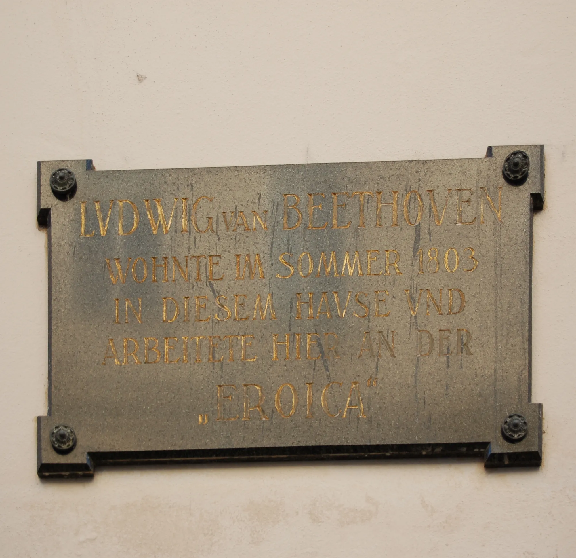 Brązowa tablica ze złotymi literami na ścianie, z napisem 'LUDWIG VAN BEETHOVEN WOHNTE IM SOMMER 1803 IN DIESEM HAUSE UND ARBEITETE HIER AN DER EROICA'