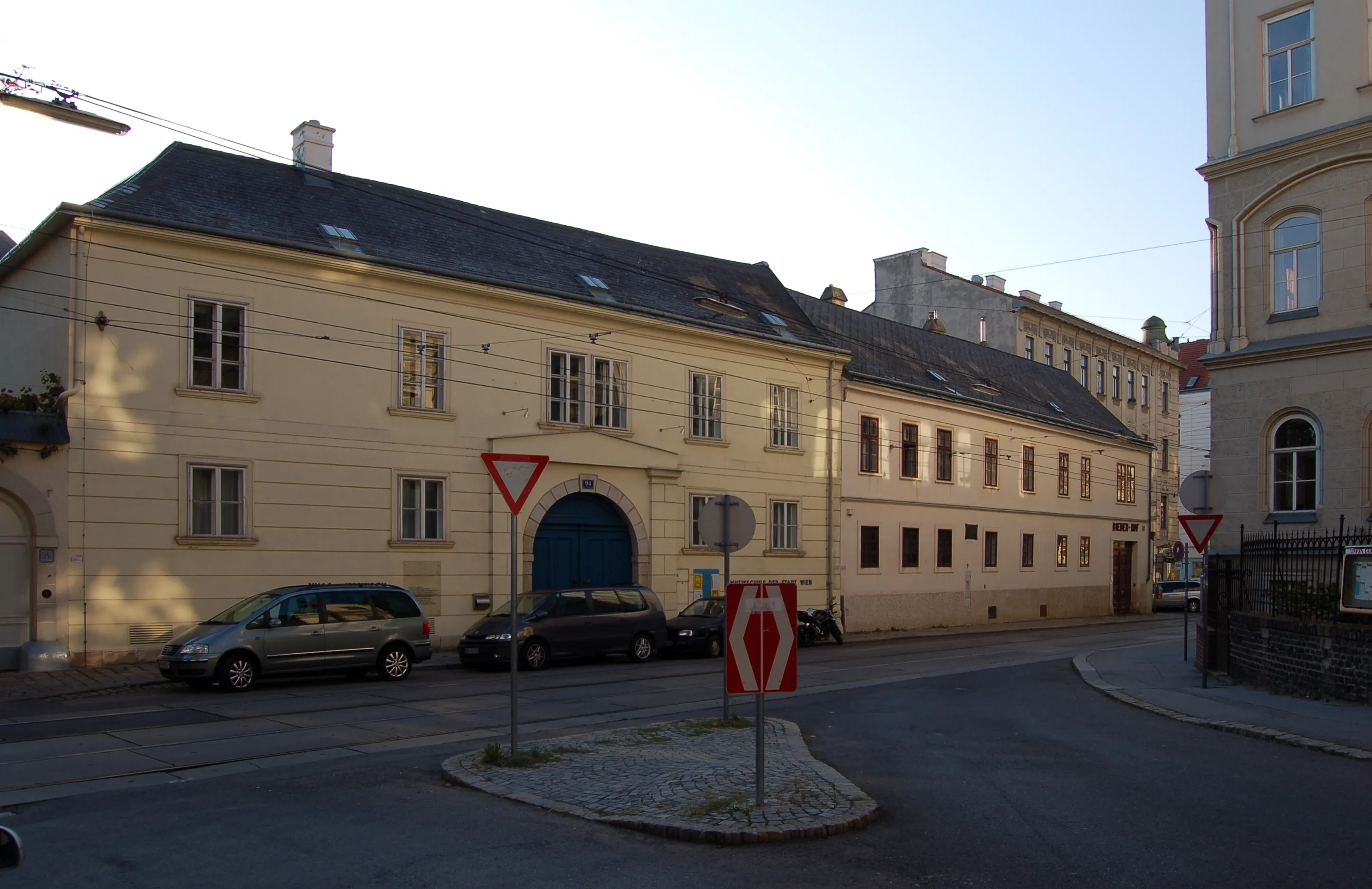 żółty budynek z łukowatym wejściem i wieloma oknami na rogu ulicy