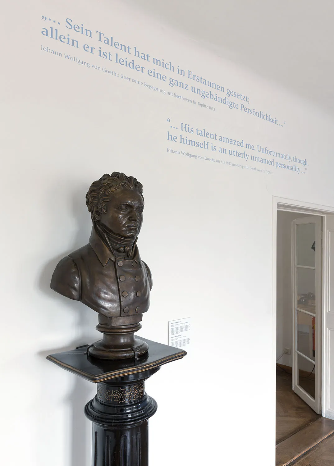 Bronze bust of Beethoven on a black pedestal with quotes on the wall