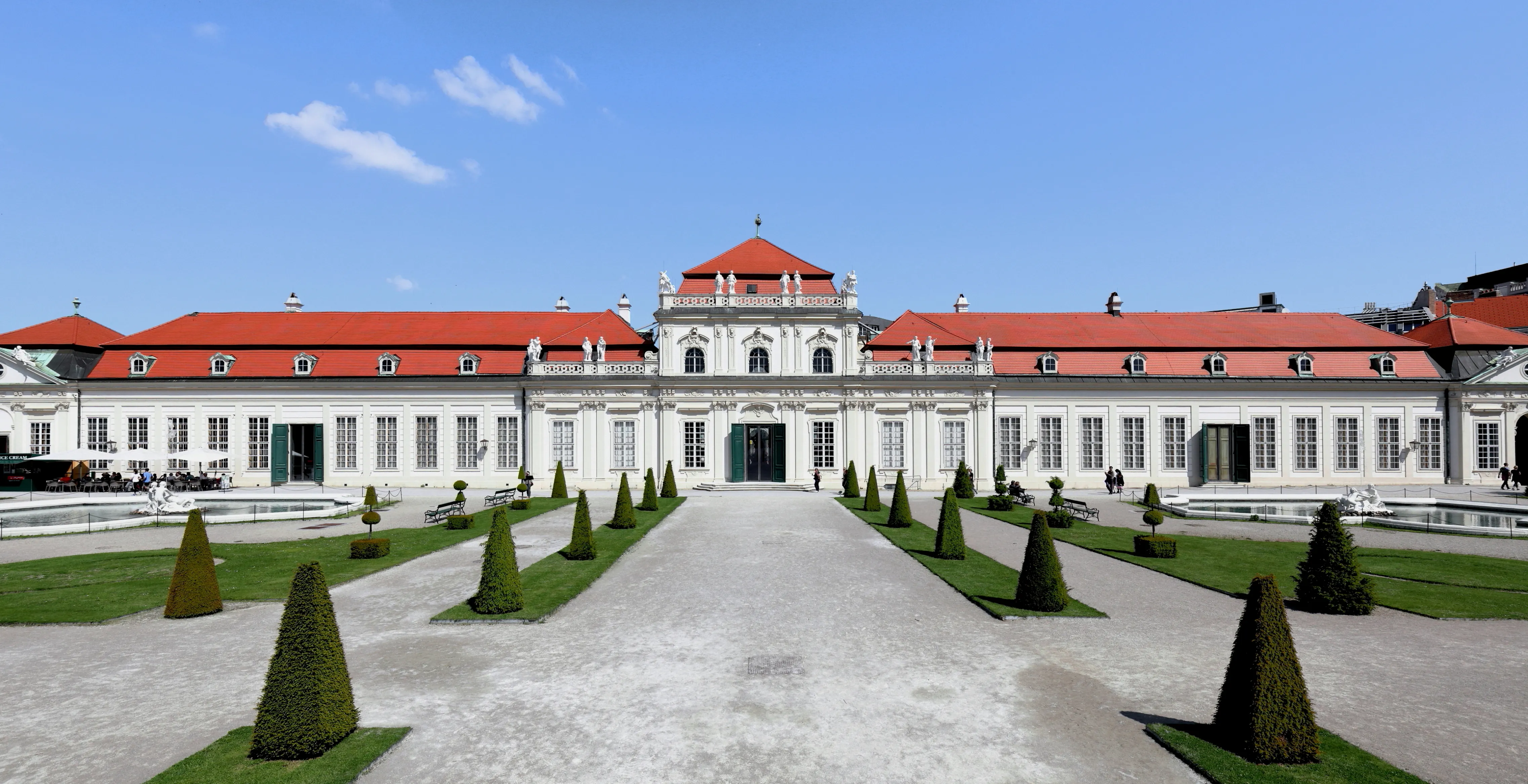 Biały pałac z czerwonym dachem i symetrycznymi ogrodami pod błękitnym niebem