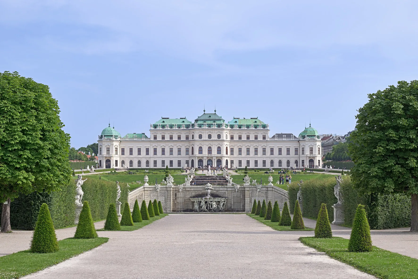 Pałac Belvedere z zielonymi kopułami i białym frontem, otoczony wypielęgnowanymi ogrodami i centralną fontanną.
