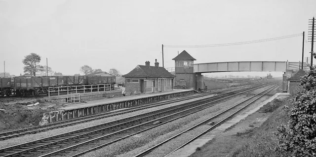 Historical black and white photograph of Beningbrough railway station showing multiple tracks, a platform, a small station building with signal box, and a pedestrian footbridge