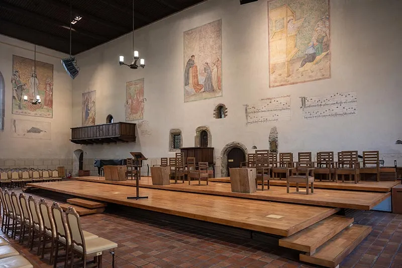 Interior de la Capilla de Belén con bancos de madera, una plataforma central y frescos en las paredes