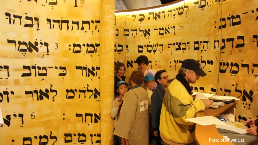 Visitors exploring an exhibition space with large Hebrew text on golden walls at Bible World Salzburg